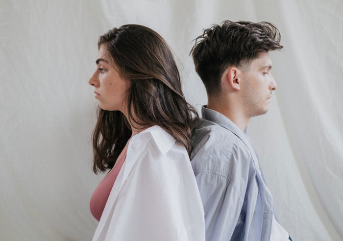 Young woman and man sitting back to back, highlighting family tension as woman doesn&rsquo;t see daughter&rsquo;s efforts.