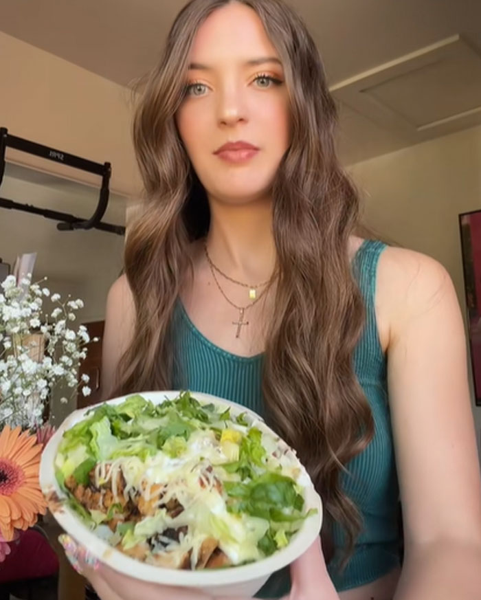 Woman holding Chipotle bowl, testing if more food is given under male names with lettuce and cheese toppings.