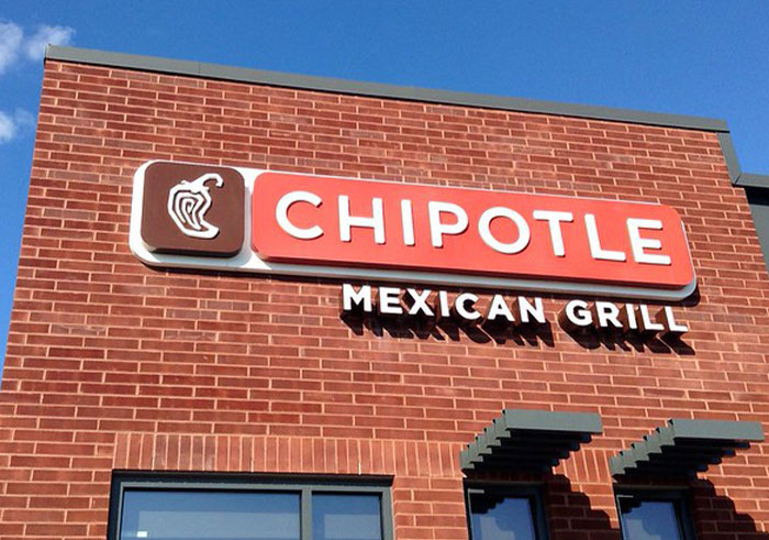 Chipotle Mexican Grill exterior sign on a brick building under a clear blue sky.