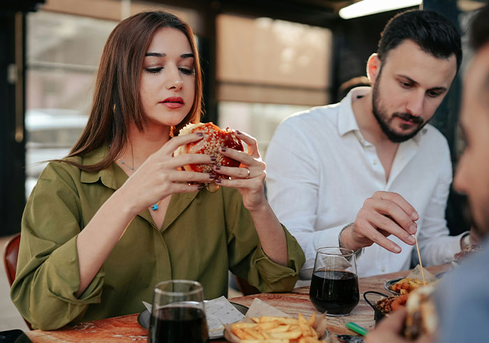 Woman holding a burger at a table with friends, testing if Chipotle adds more food to orders under male names.