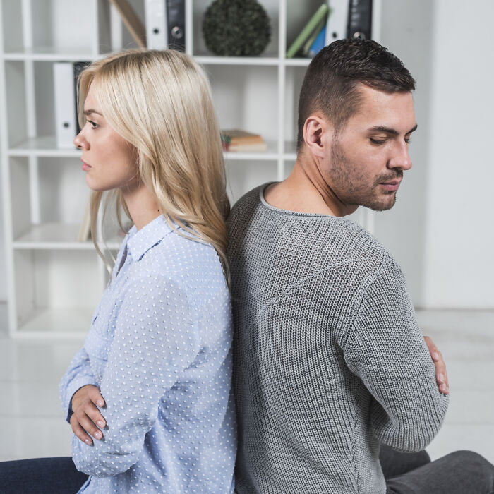 Couple sitting back to back indoors, showing tension and disagreement in a home service professional setting.