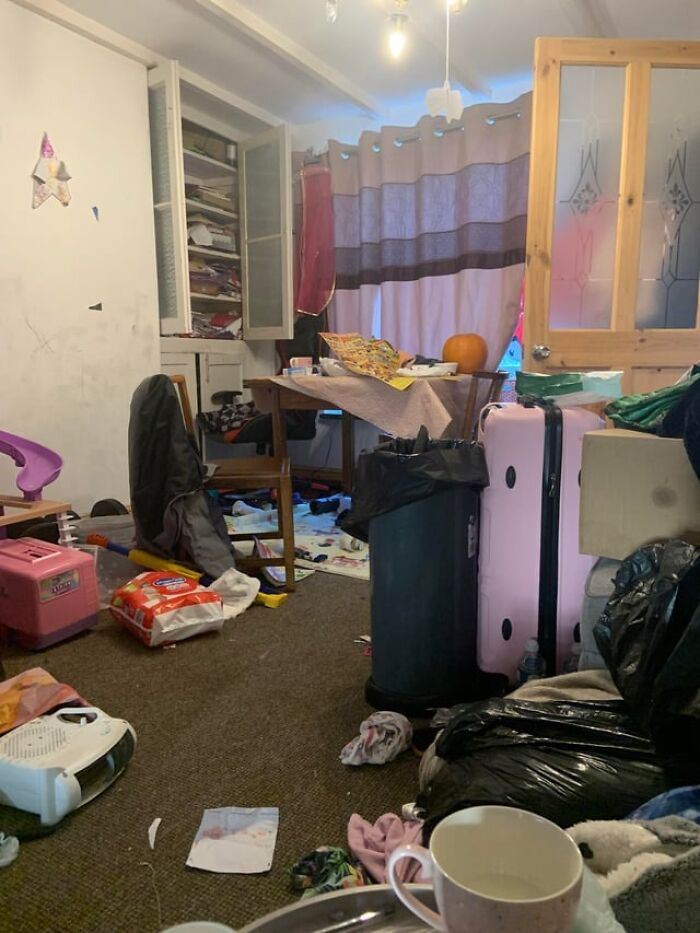 Cluttered room with scattered items, pink suitcase, and mixed household objects seen by home service professionals.