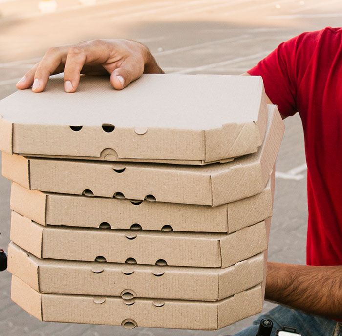 Person in red shirt holding stack of pizza boxes representing brand mistakes that led to customer boycotts.
