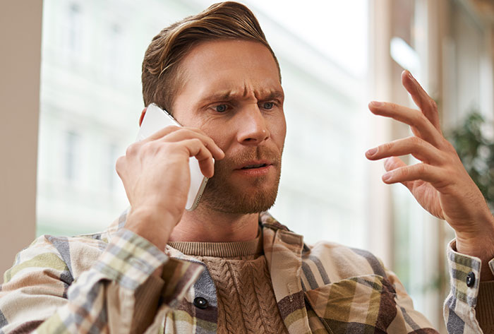 Man in a plaid shirt showing frustration while talking on phone, illustrating brand mistake and boycott reaction.