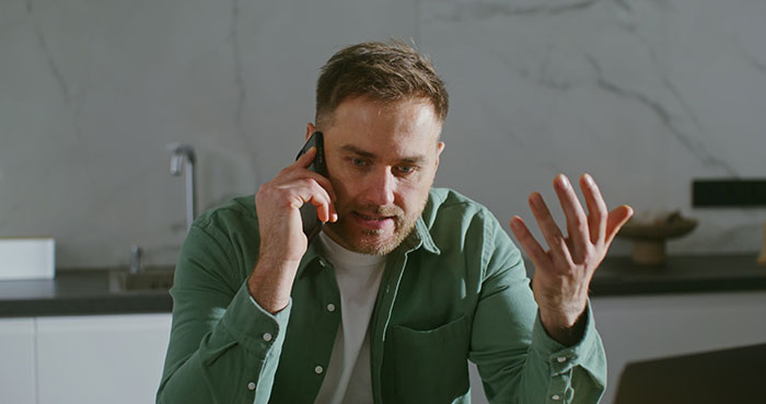 Man in green shirt talking on phone looking frustrated, illustrating brand mistake causing customer annoyance and boycott.