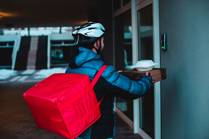 Food delivery courier with red thermal bag outside a building, illustrating brand mistakes that annoyed customers and led to boycotts.