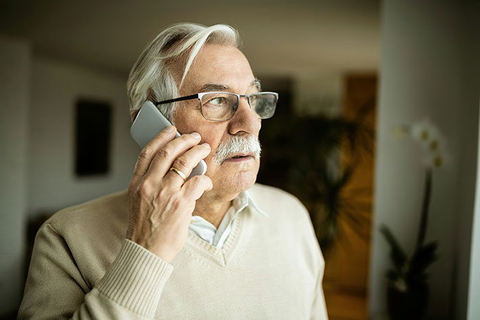 Elderly man with glasses making a phone call, illustrating brand mistake reactions leading to boycotts and customer frustration.