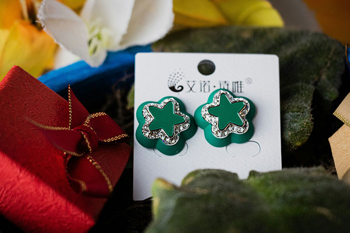 Green star-shaped earrings with rhinestones displayed on a card surrounded by gift boxes, representing worst gifts received.
