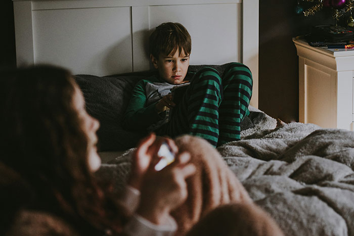 Two children in pajamas using devices on a bed, illustrating disappointment with the worst gifts received.