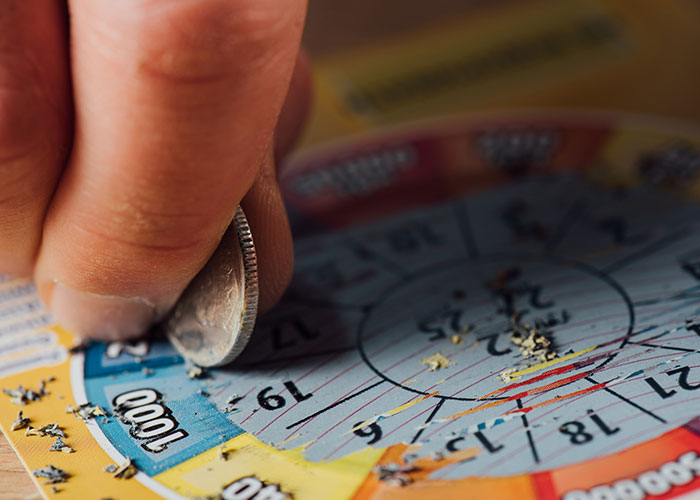 Close-up of a hand scratching a colorful lottery ticket with a coin symbolizing an insensitive or tasteless gift like a gym membership.