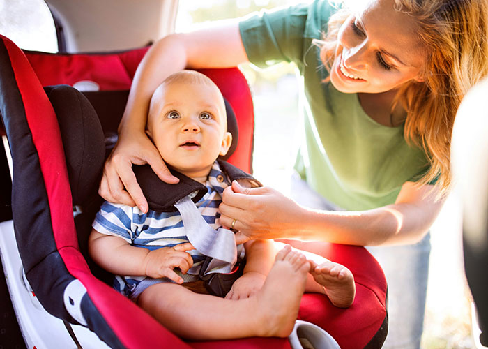 Mother securing baby in red car seat, smiling warmly while ensuring safety before a drive, highlighting family care and protection.