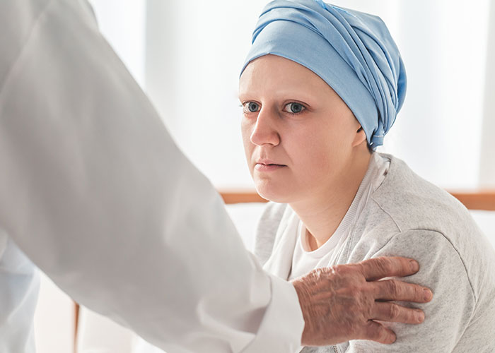Woman wearing a headscarf looks concerned while a doctor gently places a hand on her shoulder in a clinical setting.