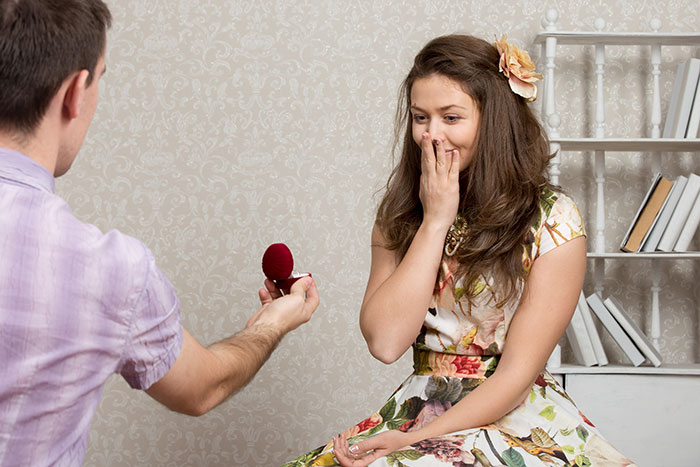 Man proposing with a ring while woman in floral dress looks surprised during a memorable proposal story moment.