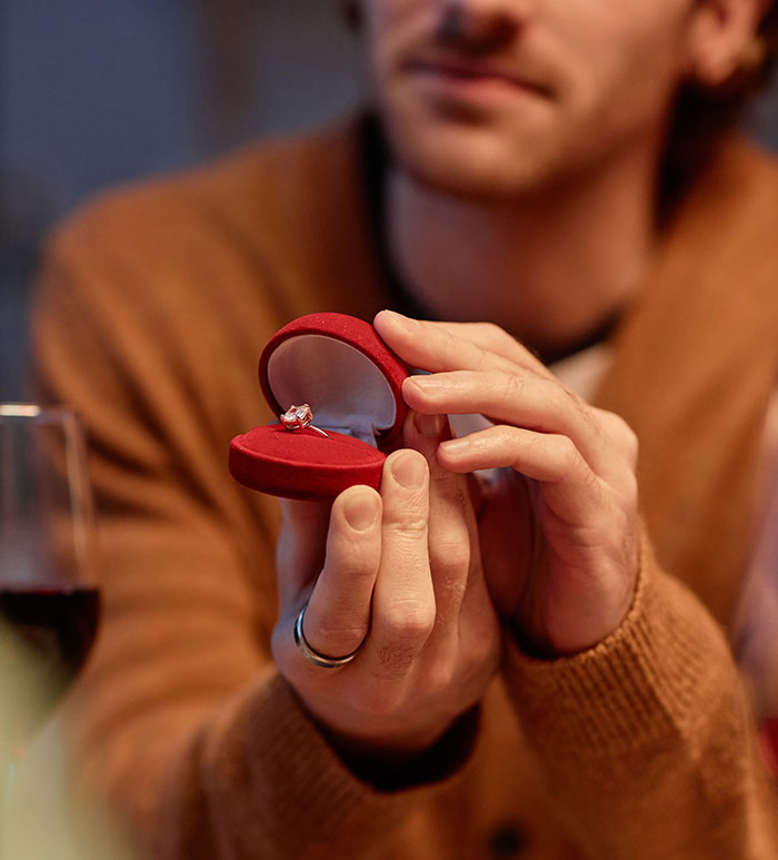 Man holding an open red ring box with an engagement ring, illustrating proposal stories that might make you side-eye your partner.