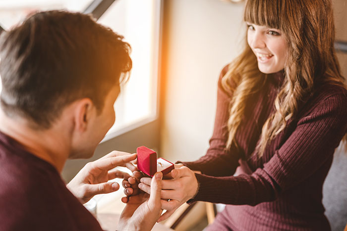 Man proposing with a ring in a red box to a smiling woman, illustrating worst proposal stories and awkward moments.