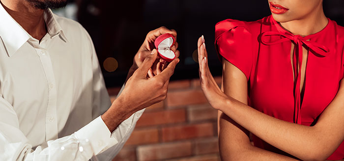 Man holding an open ring box proposing to woman who is rejecting the marriage proposal in an emotional moment.