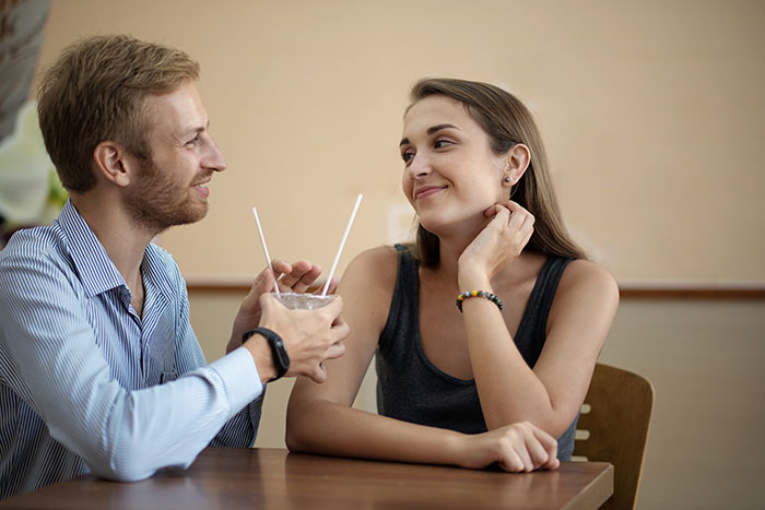 Couple sitting at a table sharing a drink, with the woman giving a side-eye glance, hinting at proposal stories.