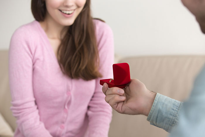 Man holding an open red ring box proposing to a smiling woman, illustrating some of the worst proposal stories.