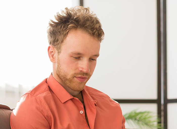 Young man in an orange shirt looking down thoughtfully, illustrating emotions from worst proposal stories.