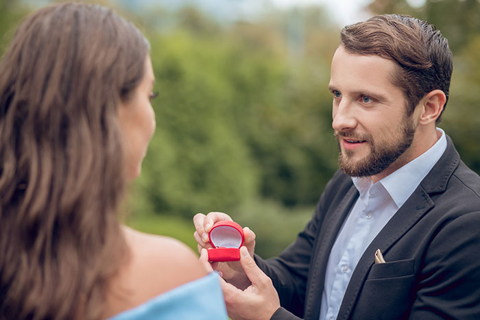 Man in a suit holding a red ring box proposing outdoors, capturing one of the worst proposal stories moments.