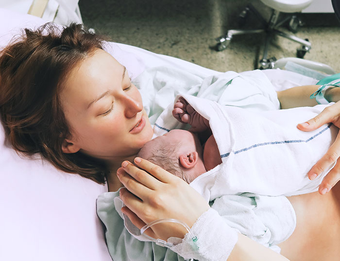New mother holding her newborn baby in hospital bed, reflecting on unexpected moments from proposal stories.