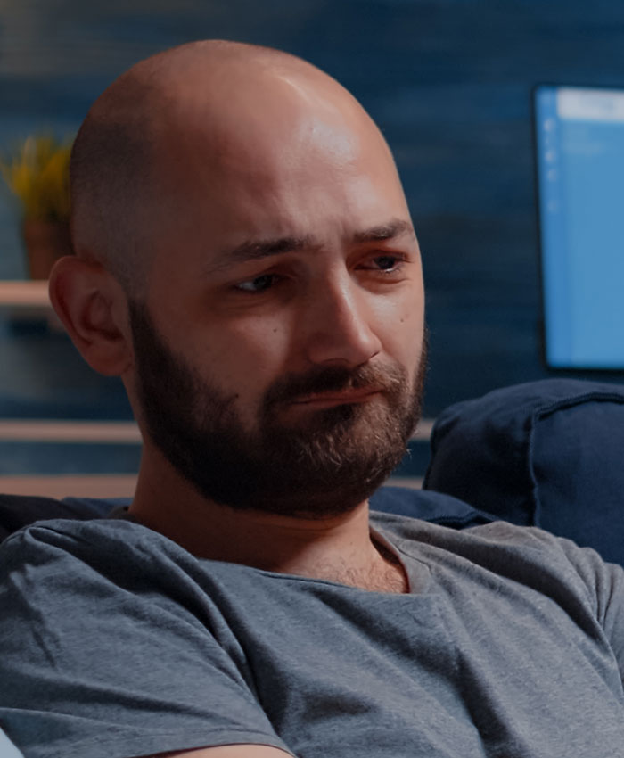 Man with beard sitting on couch looking upset, illustrating one of the worst proposal stories causing side-eye reactions.