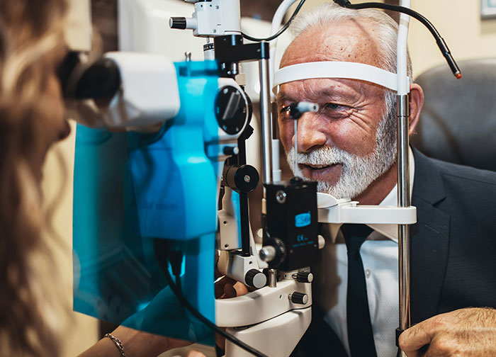 Elderly man undergoing an eye exam with a slit lamp, illustrating challenging patient experiences in healthcare settings.