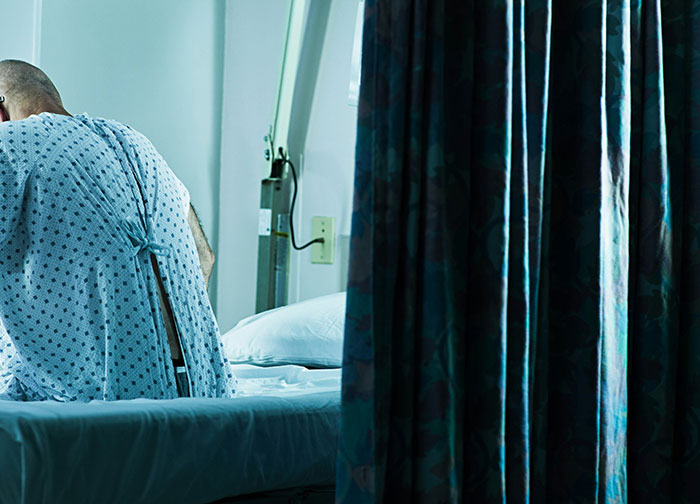 Patient in hospital gown sitting on bed, highlighting the worst things patients had to go through in hospitals.