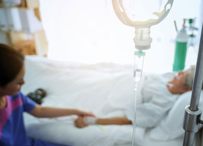 Hospital worker holding hand of a patient lying in bed with an IV drip, highlighting worst things patients endure.