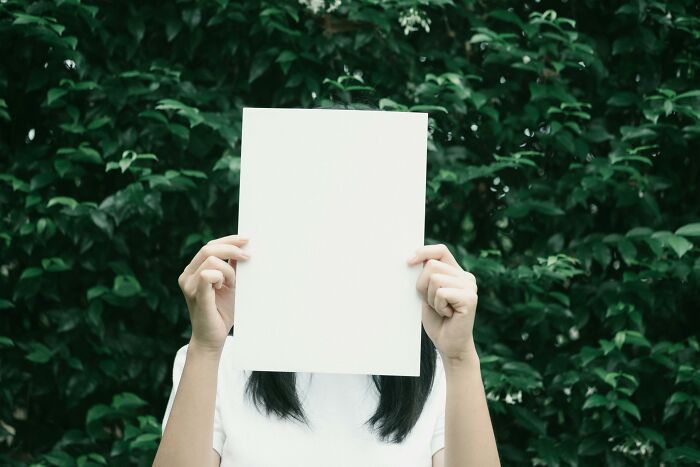 Person in white shirt holding blank paper in front of face against green foliage, symbolizing public speaking dilemma choices.