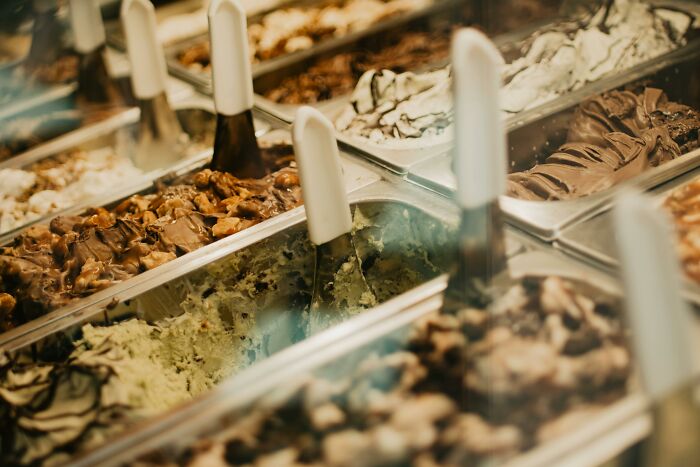 Various flavors of gelato in metal containers with scoops, highlighting the dilemma of public speaking or deep water choices.