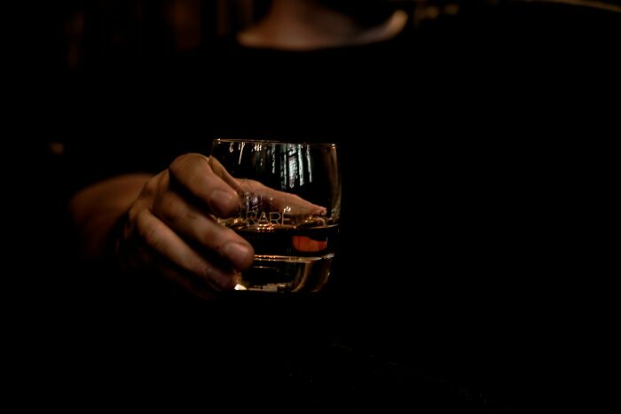 Hand holding a glass of whiskey in a dimly lit setting, illustrating unusual moments at funerals.