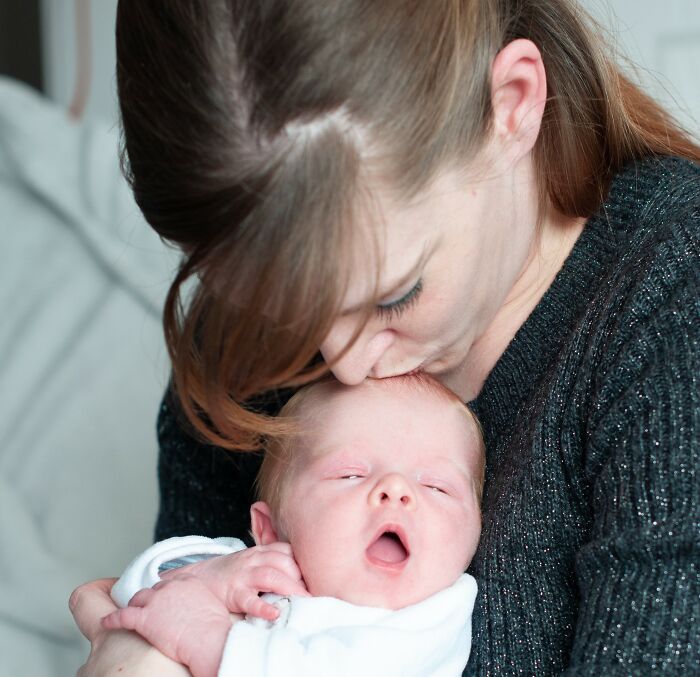 Woman holding and kissing newborn baby, highlighting stories about men and women suffering in 2025.