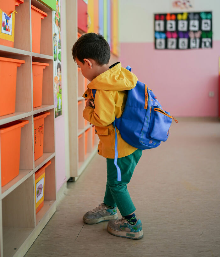 Young child with backpack in classroom surrounded by colorful bins, illustrating bizarre and weird names given to children.