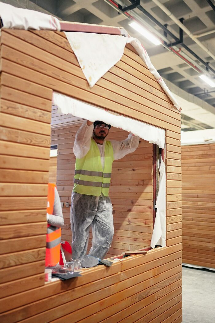 Hombre con chaleco de seguridad trabajando en construcción de cabaña de madera mostrando manifestaciones de karma instantáneo.