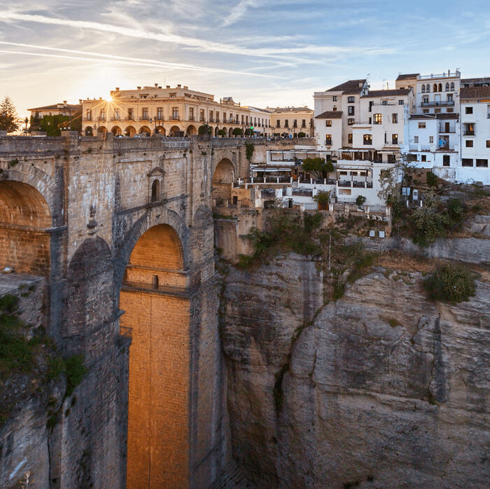 Historic stone bridge and white buildings perched on cliffs in a place from around the world that looks AI generated but is real