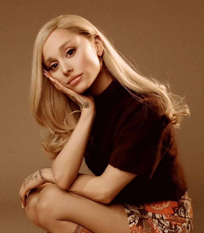 Ariana Grande posing thoughtfully in a brown top and floral skirt, linked to uncomfortable to watch performance backlash.