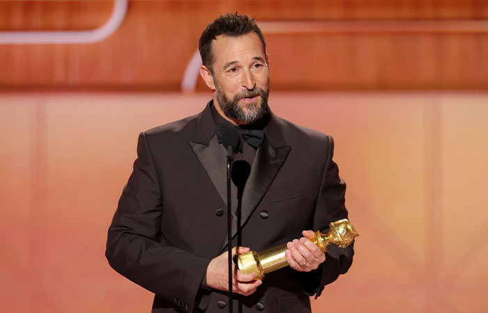 Noah Wyle in a black suit holding an award on stage, related to questions about leaving The Pitt in season 2.