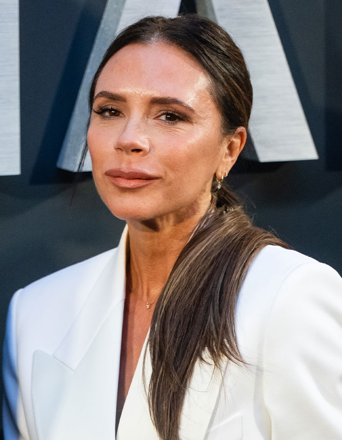 Victoria Beckham in a white blazer with long hair, posing at an event related to footage and dance accusations.