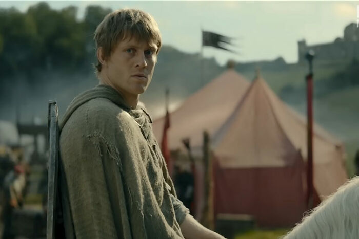 Young knight in medieval attire outdoors near a tent, representing A Knight Of The Seven Kingdoms cast member. Young knight in medieval attire outdoors near a tent, representing A Knight Of The Seven Kingdoms cast member.