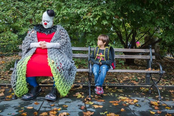 Candid street photo of a child sitting beside a clown in a park, capturing absurdity and tender moments outdoors.