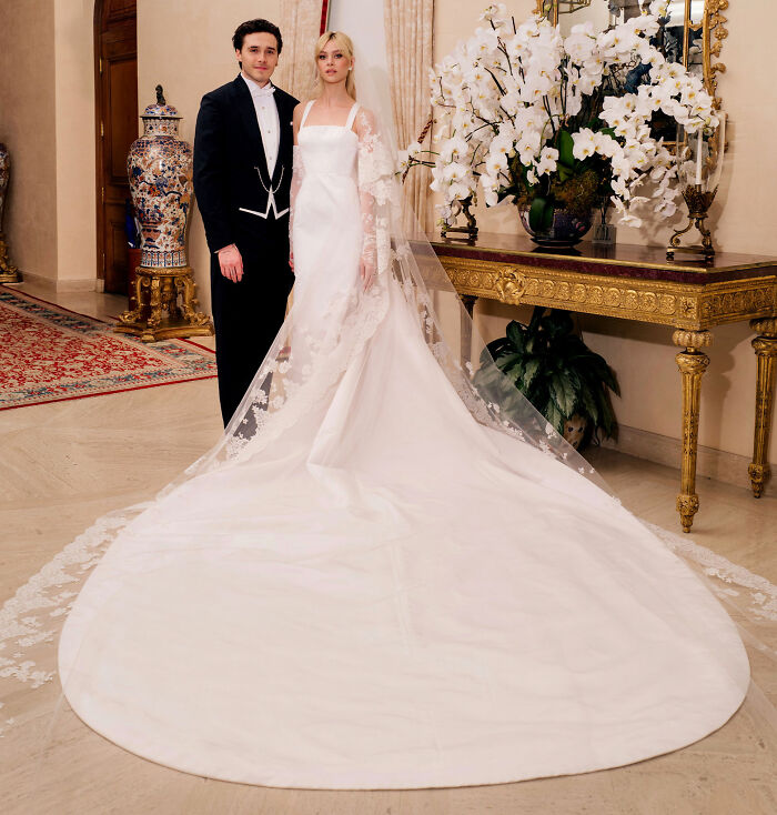 Brooklyn Beckham in formal wear with partner in wedding gown, amid luxurious indoor decor, reflecting contradiction fans discuss.