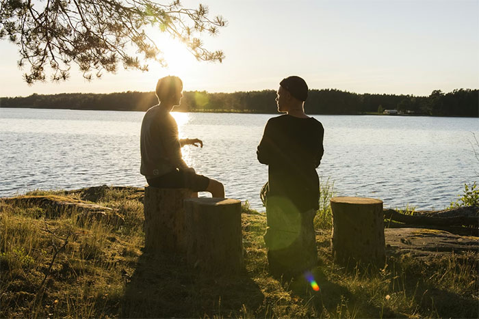 guy embarrasses wife scene: two people silhouetted by a lakeshore at sunset, one gesturing while the other listens