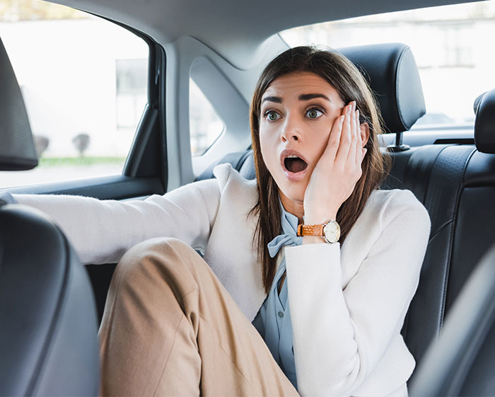 Young woman having an anxiety meltdown in the back seat of a car, illustrating risk and front seat ban.