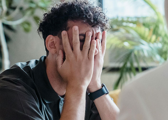 Man covering his face with hands, showing frustration and tantrum after wife refuses to do as he demands.