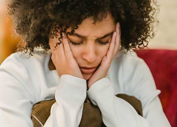 Woman looking distressed, holding her face with hands, reflecting feelings after skipping sister's birthday party event