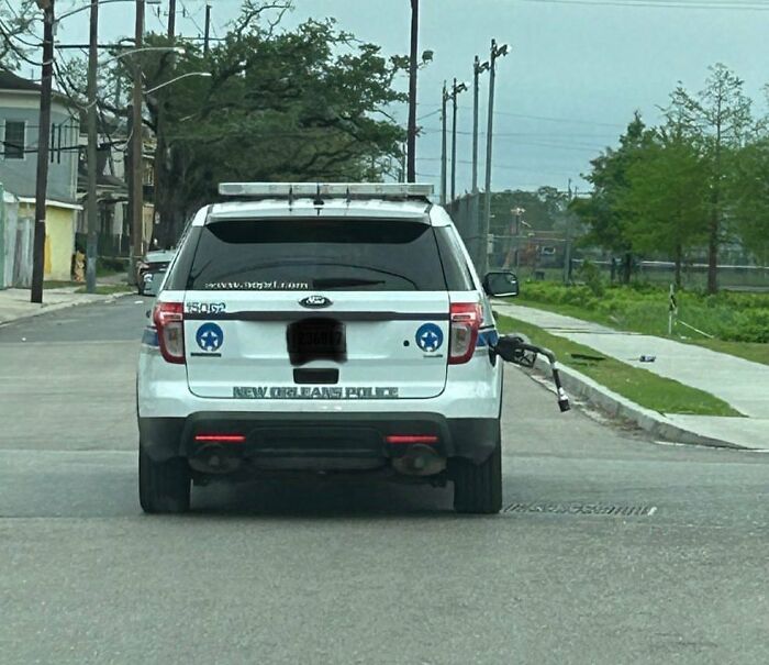 White New Orleans police SUV with a gas pump nozzle stuck in the rear right side on a city street.