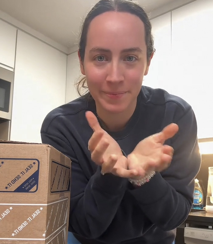 Woman in a kitchen gesturing with hands near a box, illustrating fiancé’s mug gift sparking relationship debate online. Woman in a kitchen gesturing with hands near a box, illustrating fiancé’s mug gift sparking relationship debate online.
