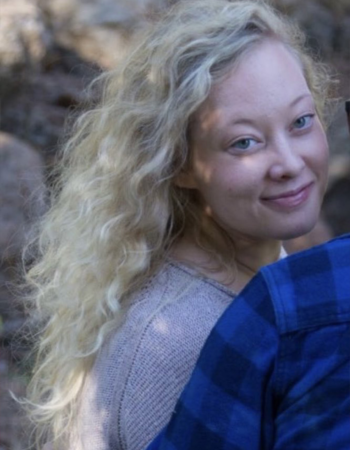 Woman with curly blonde hair smiling softly outdoors, related to Renee Good&rsquo;s wife breaking silence on fatal ICE incident.