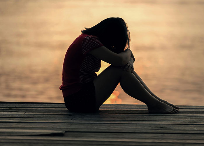 Silhouette of a person sitting alone on a wooden dock at sunset, reflecting on neurodivergent habits.